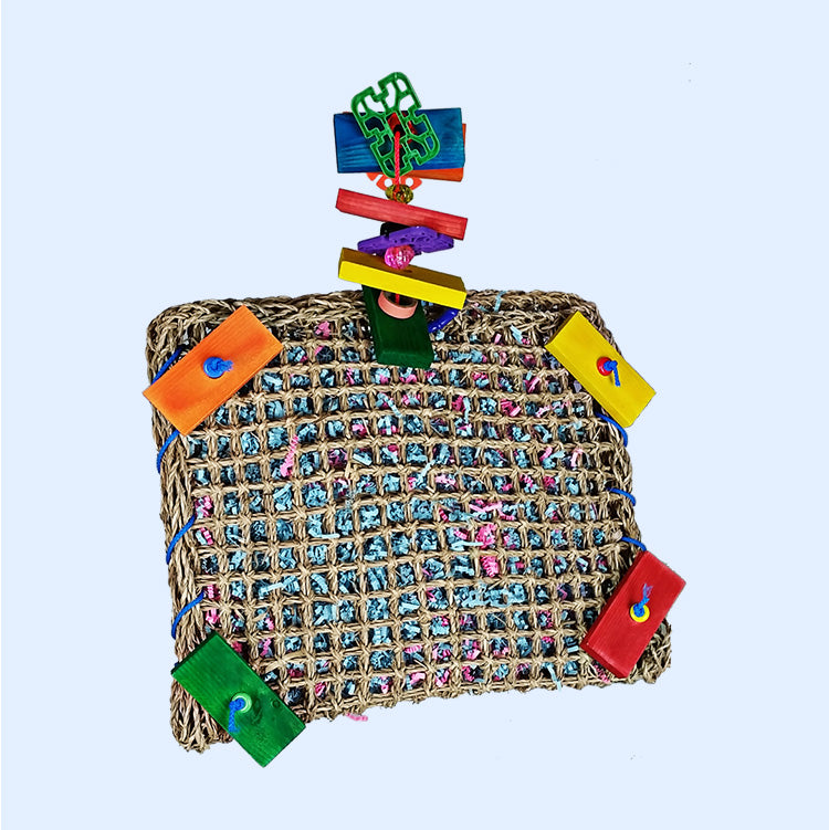 A Vine Mat Forage Pouch from Squawk Shop, featuring a woven vine mat with colorful wooden blocks and shredded paper, designed to engage birds in foraging fun.
