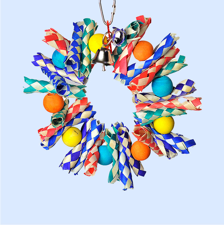 A colorful bird toy wreath made of woven bamboo, bright wooden beads, and a hanging bell in the center. Designed for parrots to chew, shred, and play. Available at Squawk Shop.