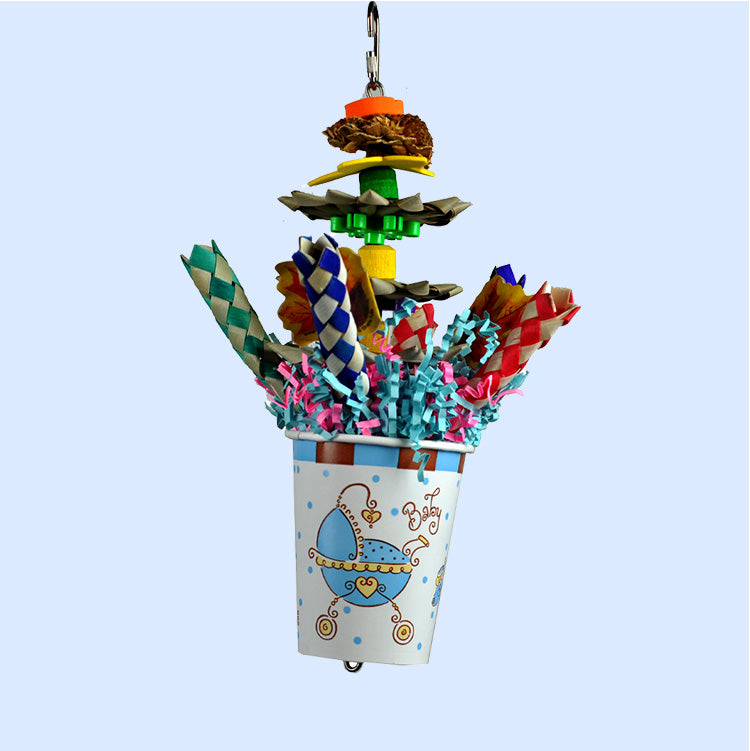 A Tropical Punch Cocktail bird toy from Squawk Shop, featuring shreddable palm leaves, colorful finger traps, crinkle paper, and wooden elements in a festive cup.