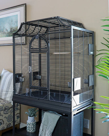 Black flight cage with arched front door, feeding bowls and seed guard, on its stand in a living room